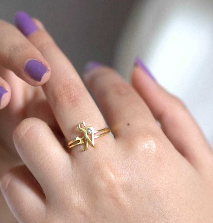 Hand wearing a gold ring with a star design, against a neutral background.