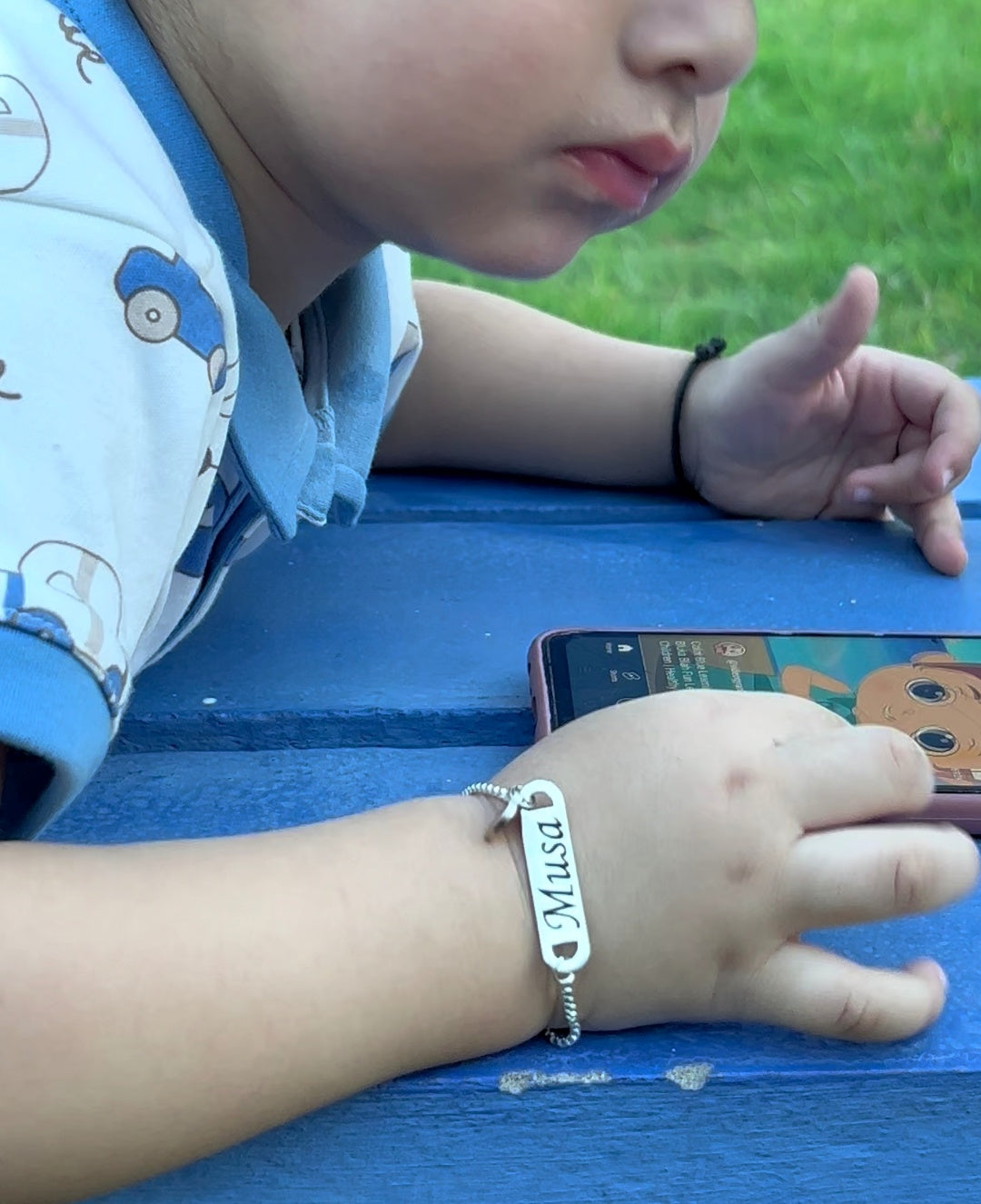 Child wearing a bracelet with 'Musa' on it, sitting outdoors.