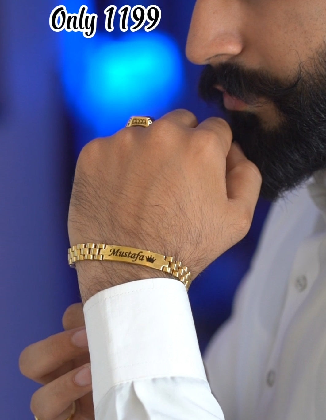 Man wearing a gold bracelet with 'Mustafa' engraved on it against a blue background.