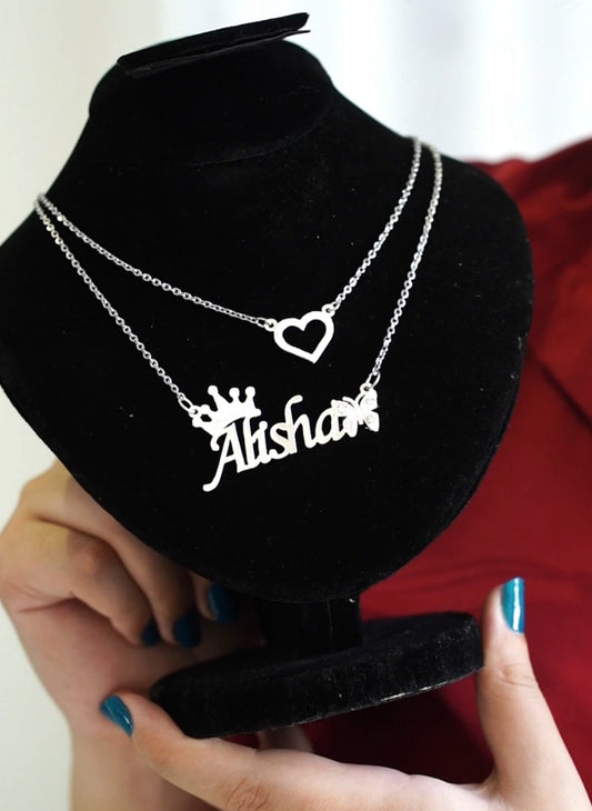 Necklace with 'Alisha' name pendant on a black stand, held by hands with red garment in background.